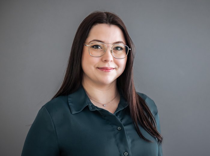 Porträt einer jungen Frau, Daria Gutowska, mit langen, dunklen Haaren und einer Brille mit goldfarbenem Rahmen. Sie trägt eine dunkelgrüne Bluse und lächelt dezent in die Kamera. 